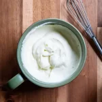 A mug with garlic aioli dip in it and a whisk next to it.