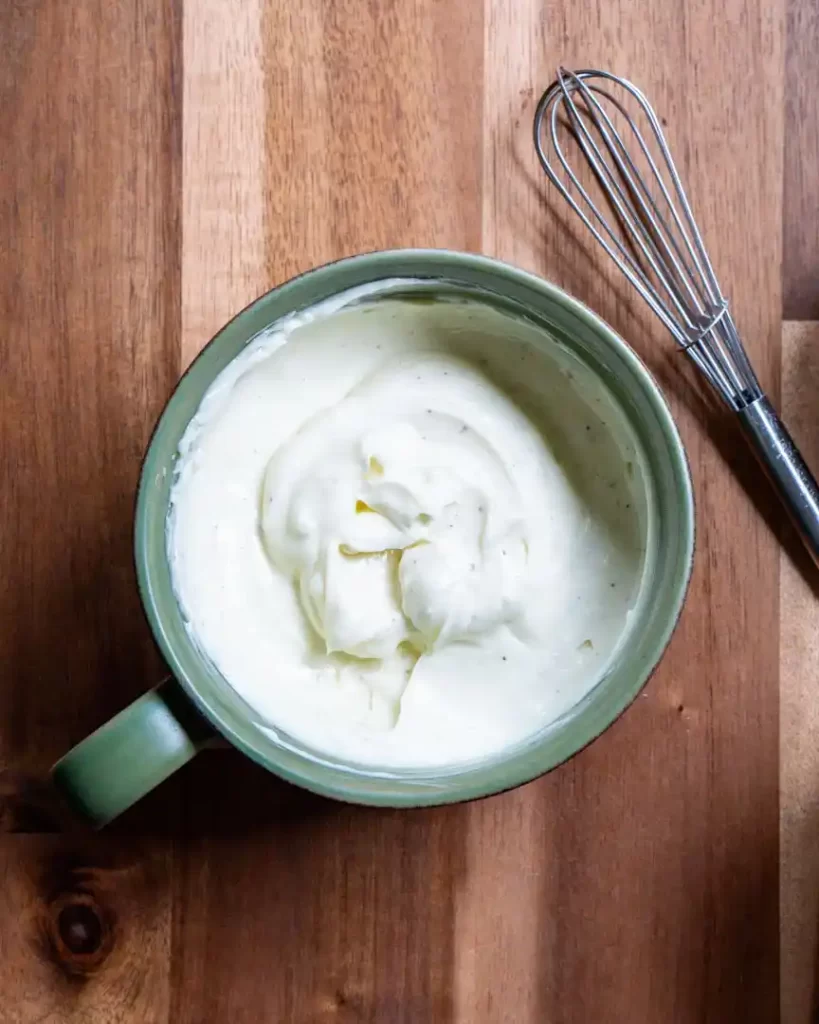 A mug with garlic aioli dip in it and a whisk next to it.