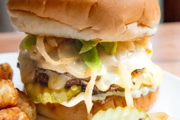 A smash burger with all the toppings and pickles on the plate next to the burger.