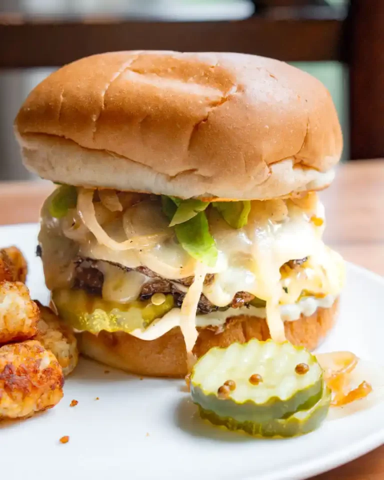 A smash burger with all the toppings and pickles on the plate next to the burger.