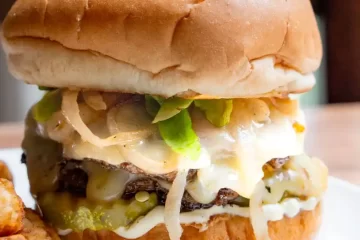 A burger on a plate with caramelized onions, lettuce and cheese peaking out.