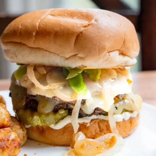 A burger on a plate with caramelized onions, lettuce and cheese peaking out.