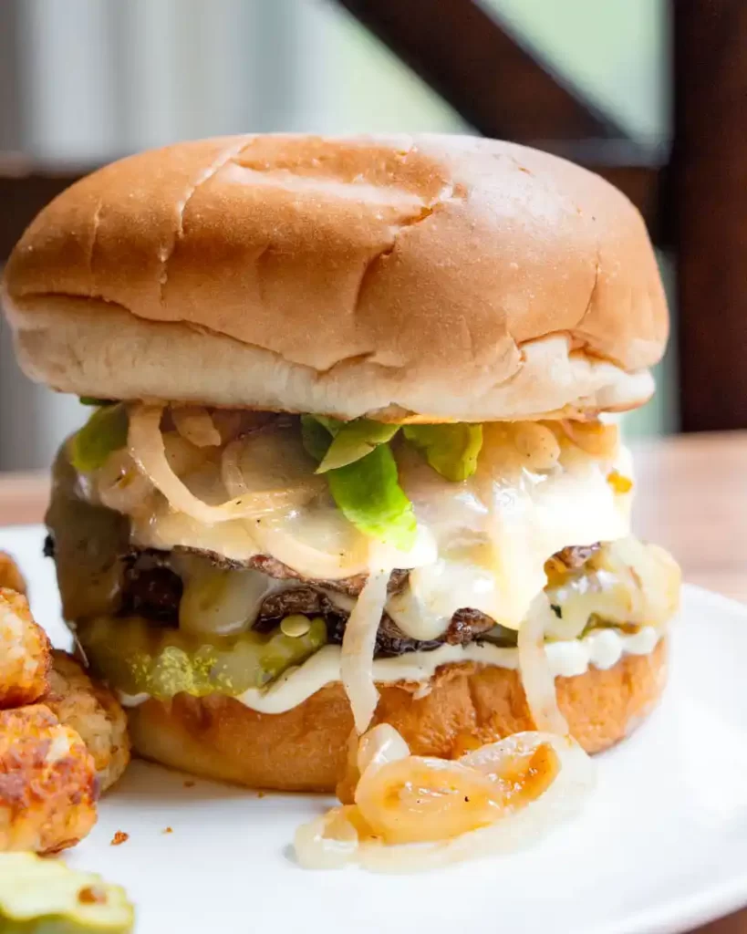 A burger on a plate with caramelized onions, lettuce and cheese peaking out.