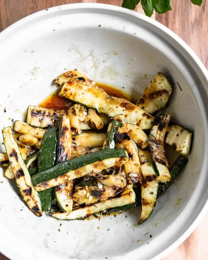 A bowl of grilled zucchini spears in its juices.