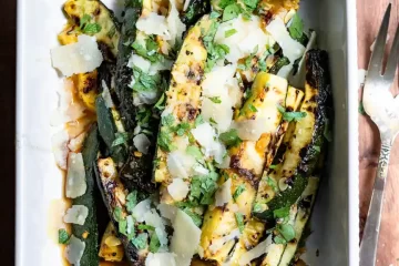 Grilled zucchini spears topped with parmesan cheese shavings and minced fresh parsley in a serving dish.