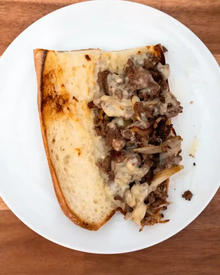 Open faced sandwich with a long toasted bun and fried onions and ground beef on the bun. The sandwich is on a plate.