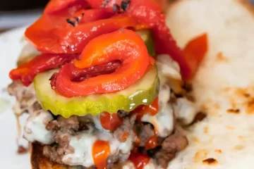 Open faced sandwich with ground beef, melted American cheese, pickles, peppers, and ketchup on top of it.