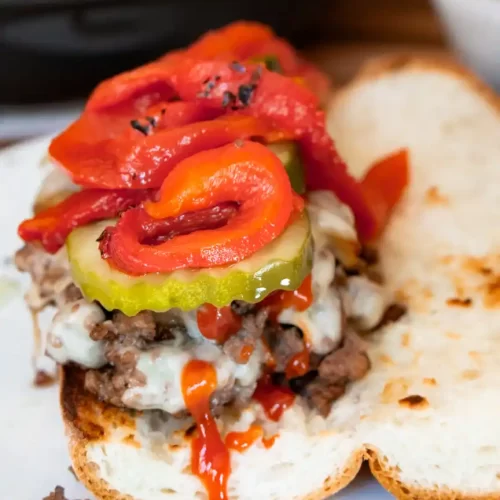 Open faced sandwich with ground beef, melted American cheese, pickles, peppers, and ketchup on top of it.