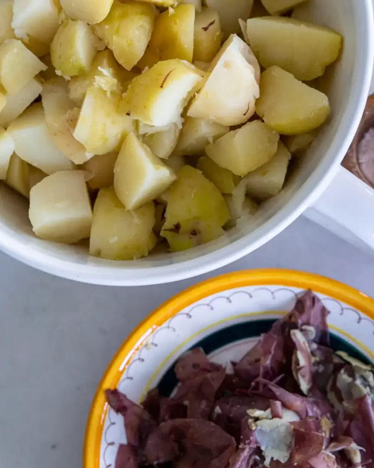 A bowl with peeled boiled potato chunks. There is a smaller bowl next to it and it has the potato skins in it.