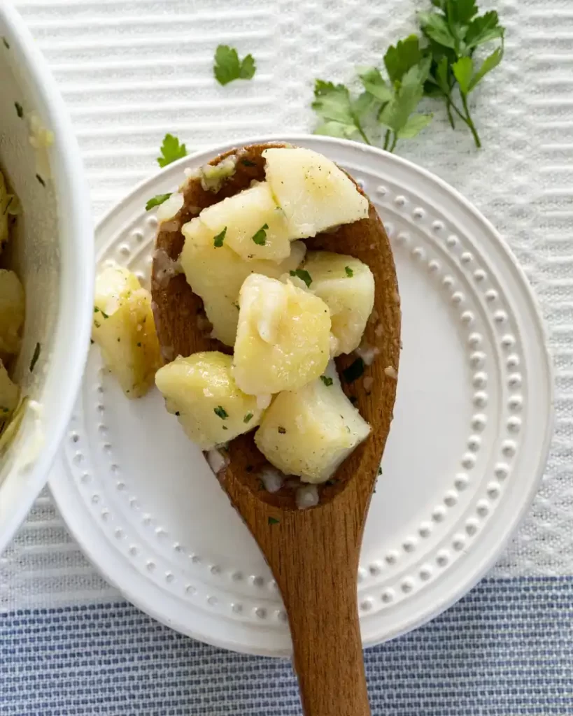 A wooden spoon on a small plate. The wooden spoon has a scoop of boiled potatoes on it.