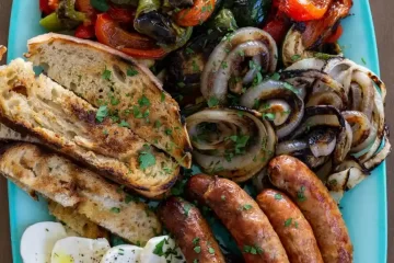 A platter filled with grilled veggies, grilled sausages, sliced mozzarella cheese, and sliced toasted bread.