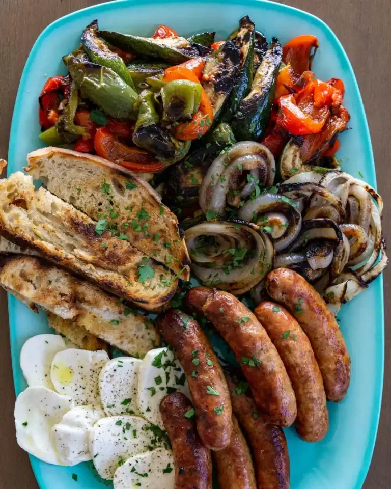 A platter filled with grilled veggies, grilled sausages, sliced mozzarella cheese, and sliced toasted bread.