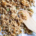 Lemon Pistachio Granola on a baking sheet with a wood spatula on top of the granola