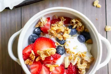 A bowl of yogurt with fresh blueberries, strawberries and granola on top.