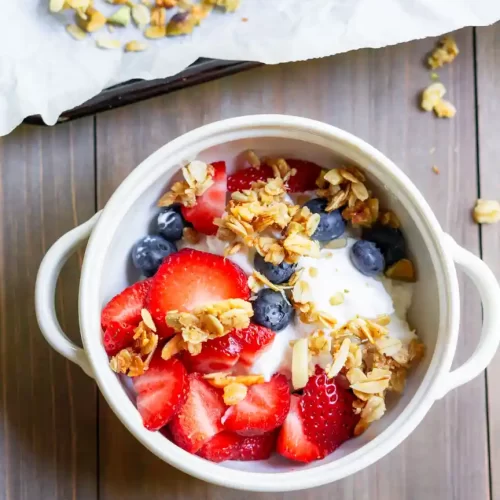 A bowl of yogurt with fresh blueberries, strawberries and granola on top.