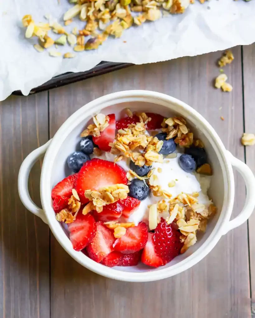 A bowl of yogurt with fresh blueberries, strawberries and granola on top.