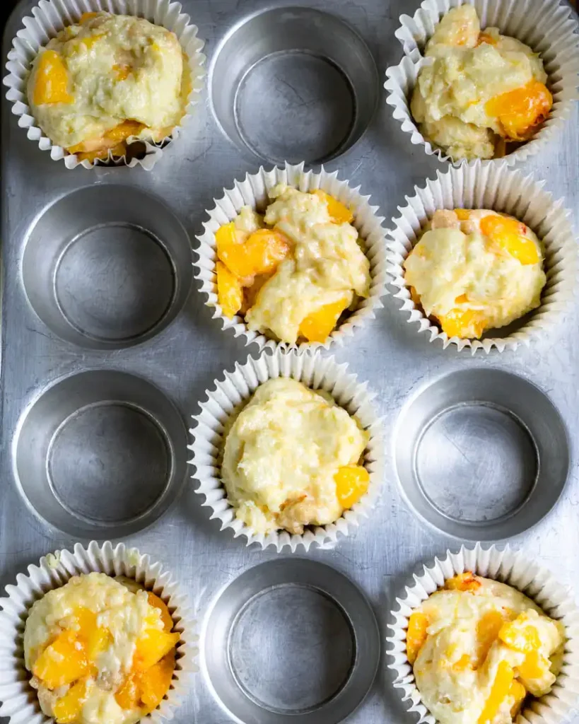 A muffin pan with unbaked peach muffins.