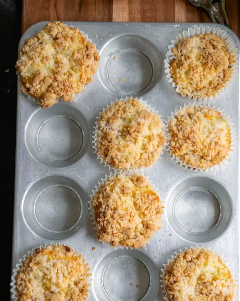 A muffin pan with baked gluten-free peach muffins with streusel topping.