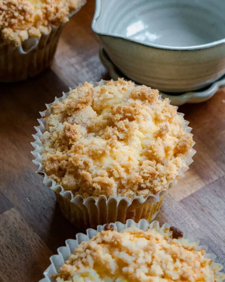 Gluten-free peach muffins on a wooden board. There is mini bowl behind one of the muffins.