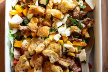 Grilled chicken and peach salad in a rectangle baking pan with a wooden spoon.