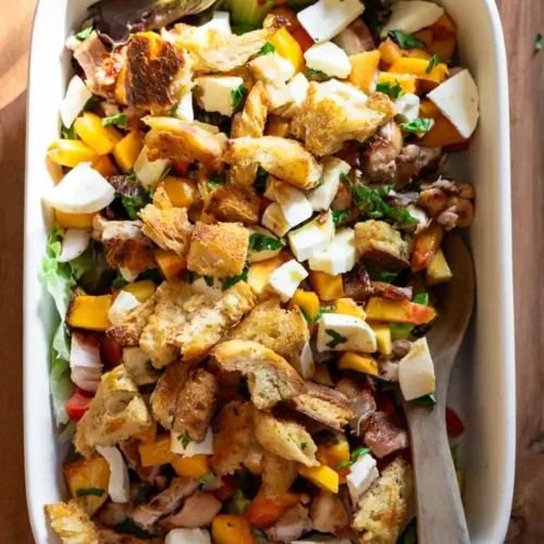 Grilled chicken and peach salad in a rectangle baking pan with a wooden spoon.