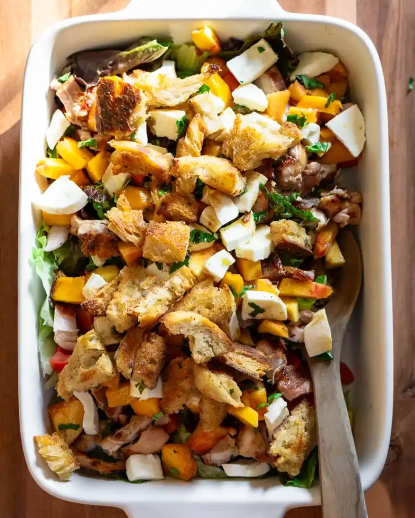 Grilled chicken and peach salad in a rectangle baking pan with a wooden spoon.