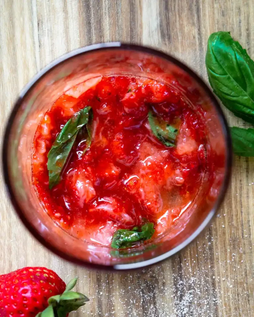 A top down view of muddled strawberries and basil in a glass.