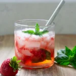 A short glass with strawberry basil spritzer mocktail in it. The glass has a short stainless steel straw in it.