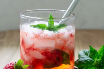 A short glass with strawberry basil spritzer mocktail in it. The glass has a short stainless steel straw in it.