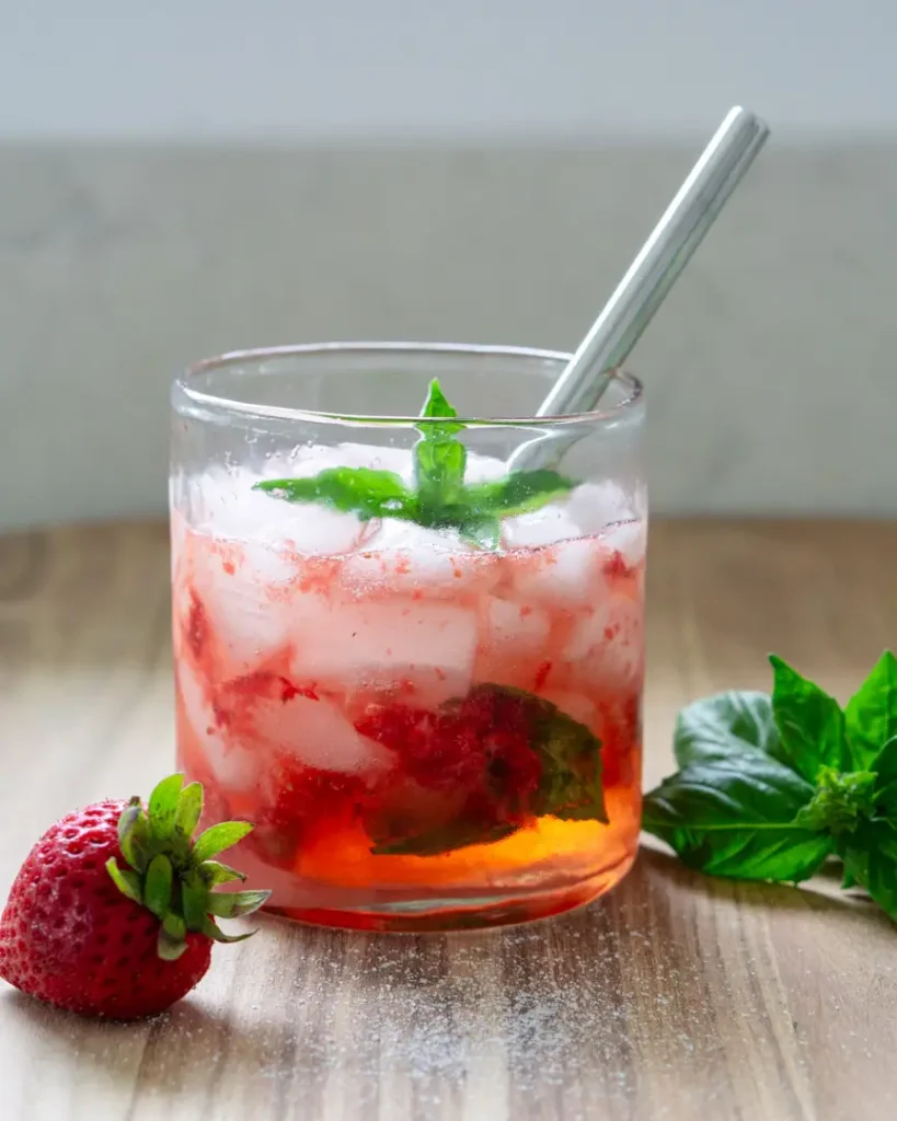 A short glass with strawberry basil spritzer mocktail in it. The glass has a short stainless steel straw in it.