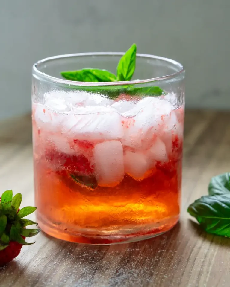 A short glass with strawberry basil spritzer mocktail that's topped with a basil sprig.