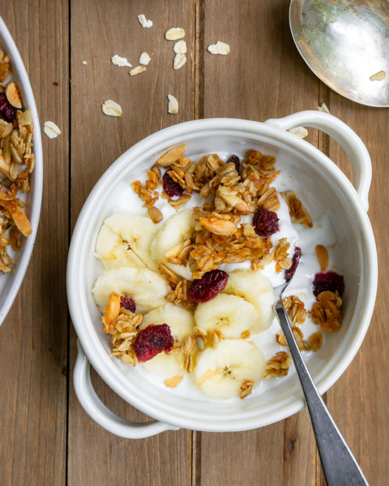 A bowl of yogurt with cherry and almond granola and banana topping.