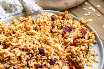 A plate with cherry & almond granola on it. There is a spoon on the plate with granola on it.