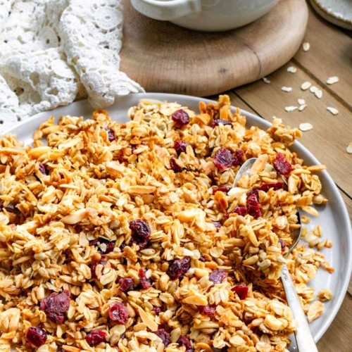 A plate with cherry & almond granola on it. There is a spoon on the plate with granola on it.