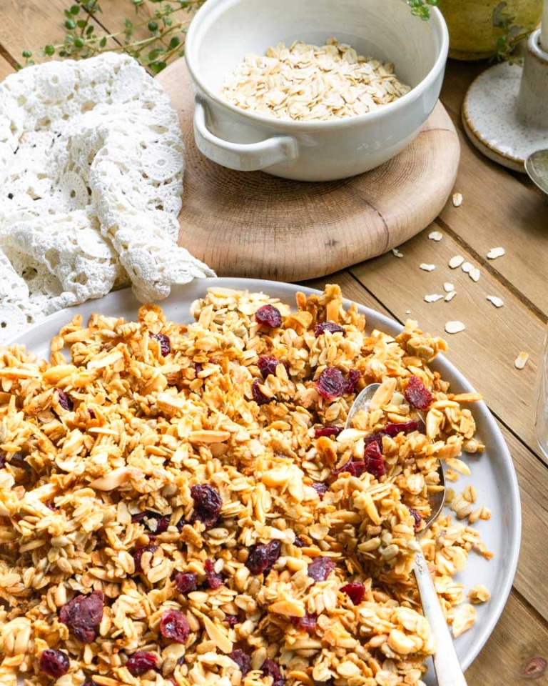 A plate of granola with a spoon. There is a bowl of raw oats next to it.