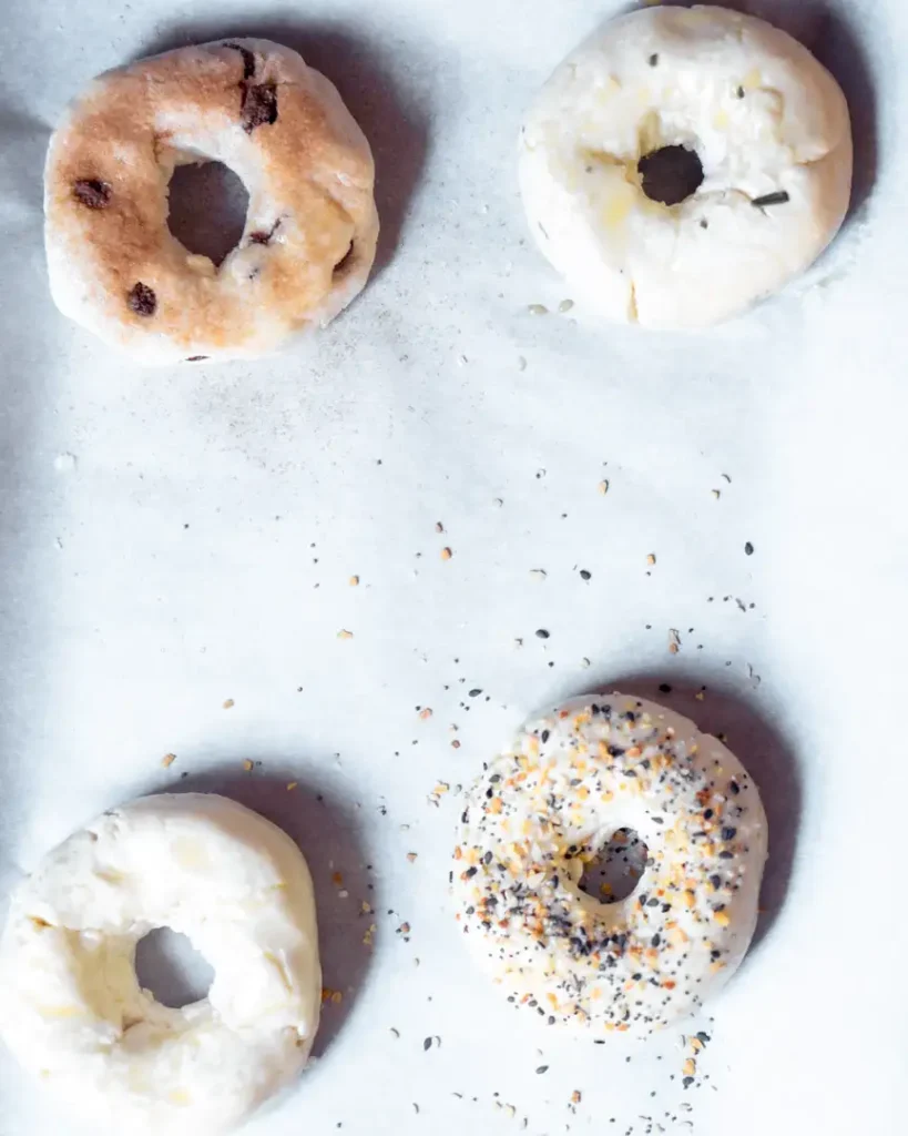 Unbaked assorted bagels on a baking sheet.