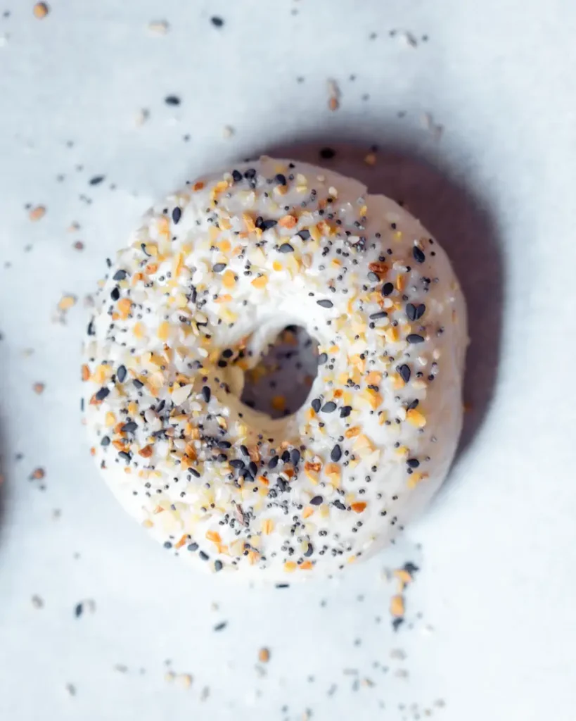 An uncooked bagel with everything bagel seasoning on top.