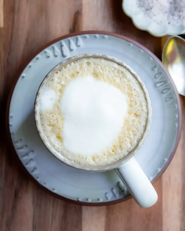 Top down view of a mug on a plate. The mug is filled with a latte and it's top is frothed.