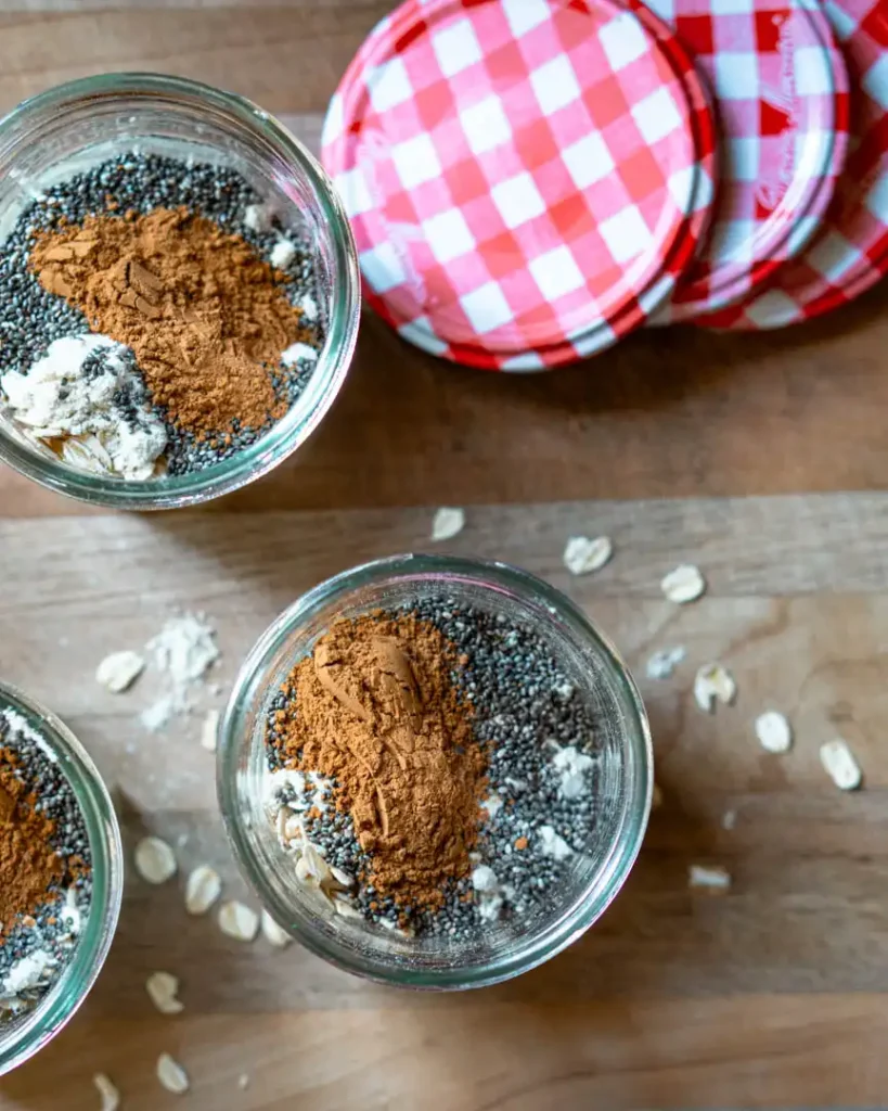 Top down view into 2 jars filled with dried oats, chia seeds and spices.