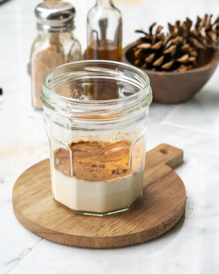 A glass jar with milk and spices laying on top of the milk ready to be stirred in.