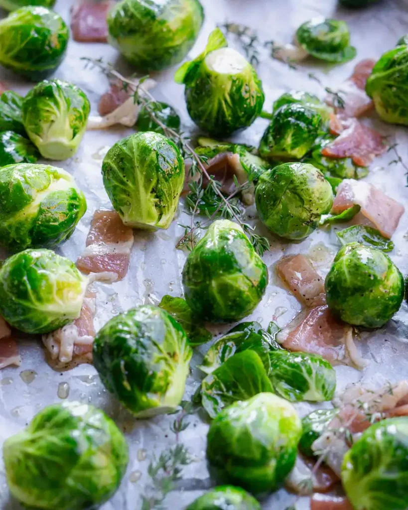 Raw brussel sprouts and bite size strips of uncooked bacon on a bacon tray.