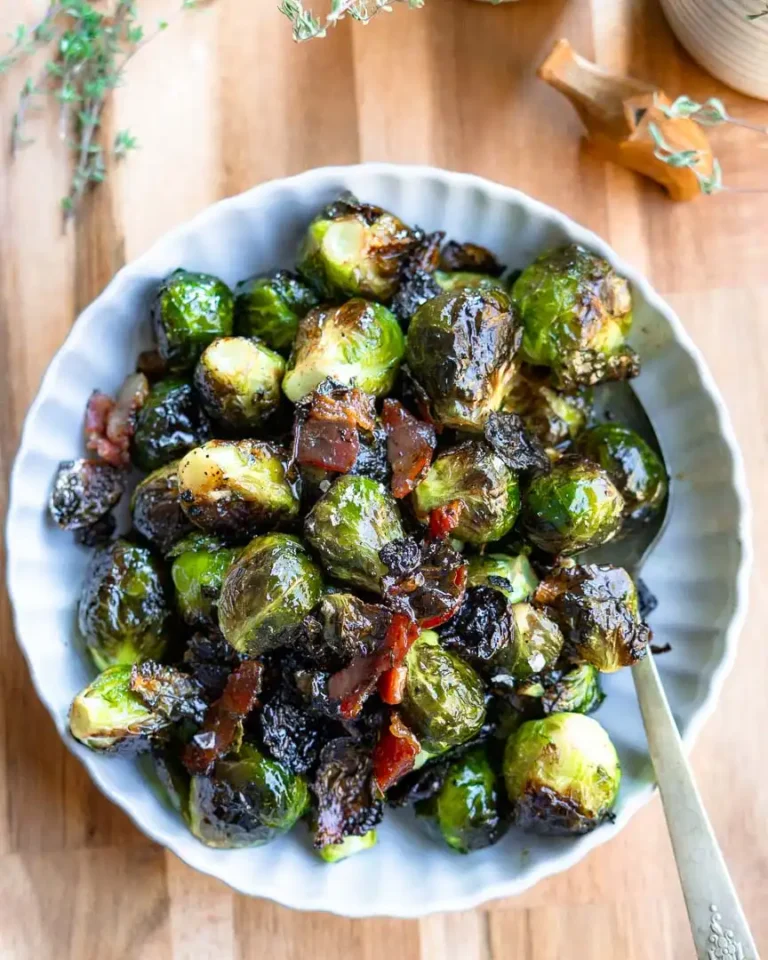 Roasted brussels sprouts and bacon in a scalloped bowl. There is a serving spoon in the bowl for serving.