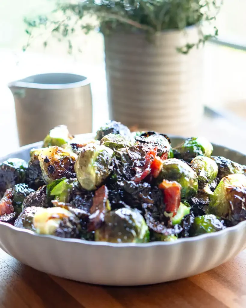 Roasted brussels sprouts with bacon in a bowl. There is pitcher filled with dried thyme behind it.