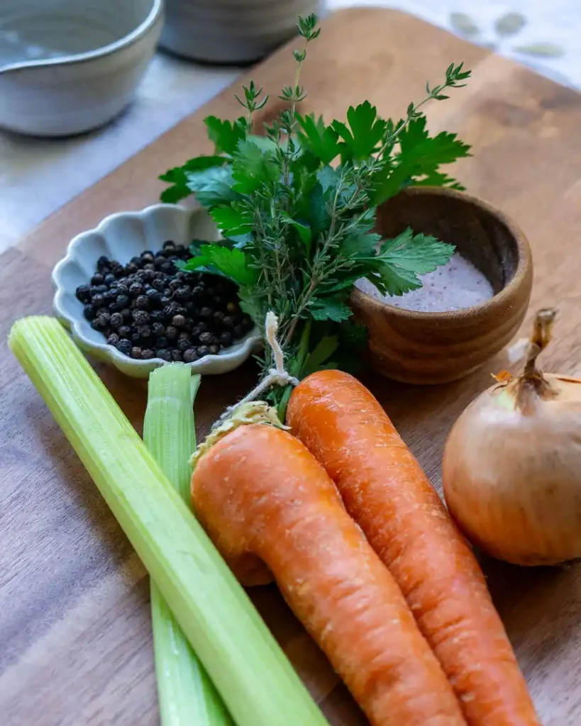 Raw carrots, celery, onion and spices on a cutting board.