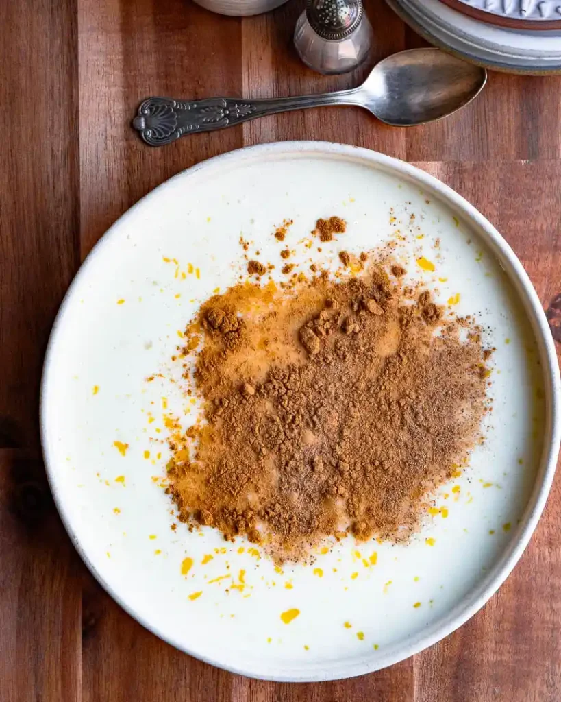 Spices on top of eggnog in a shallow bowl.