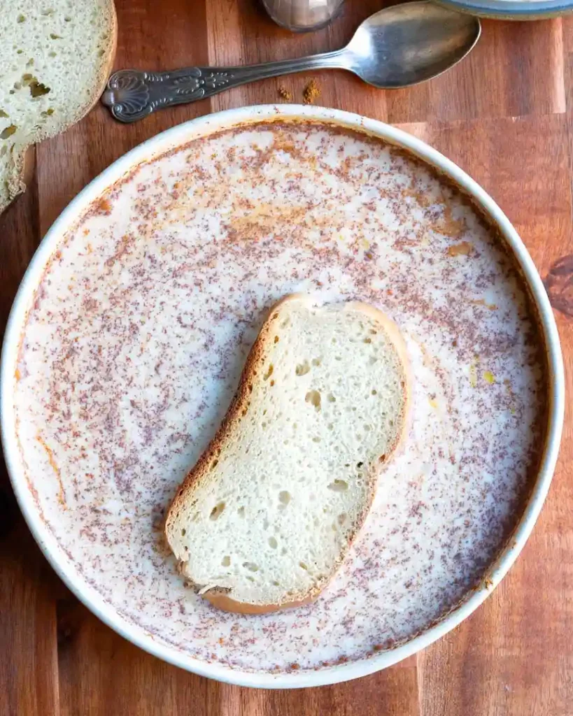 A slice of bread in a bowl of eggnog mixed with spices.