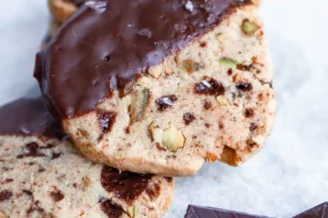 A gluten free shortbread cookie half dipped in chocolate on top of a stack of similar cookies.