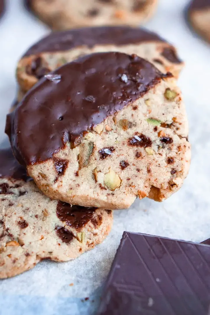 A gluten free shortbread cookie half dipped in chocolate on top of a stack of similar cookies.