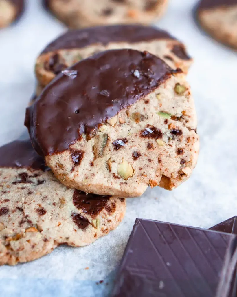 A gluten free shortbread cookie half dipped in chocolate on top of a stack of similar cookies.