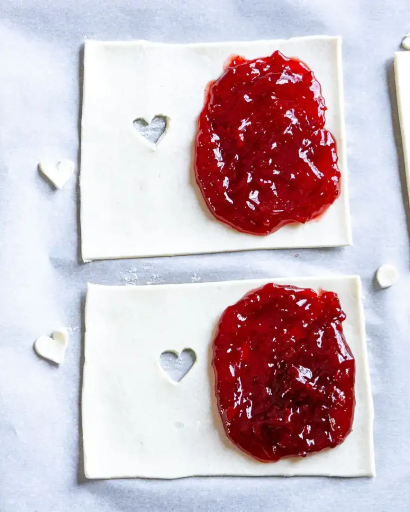 Unbaked and unfolded cherry turnover with one side piled with cherry filling and the other side has a heart cut out in the middle of it.